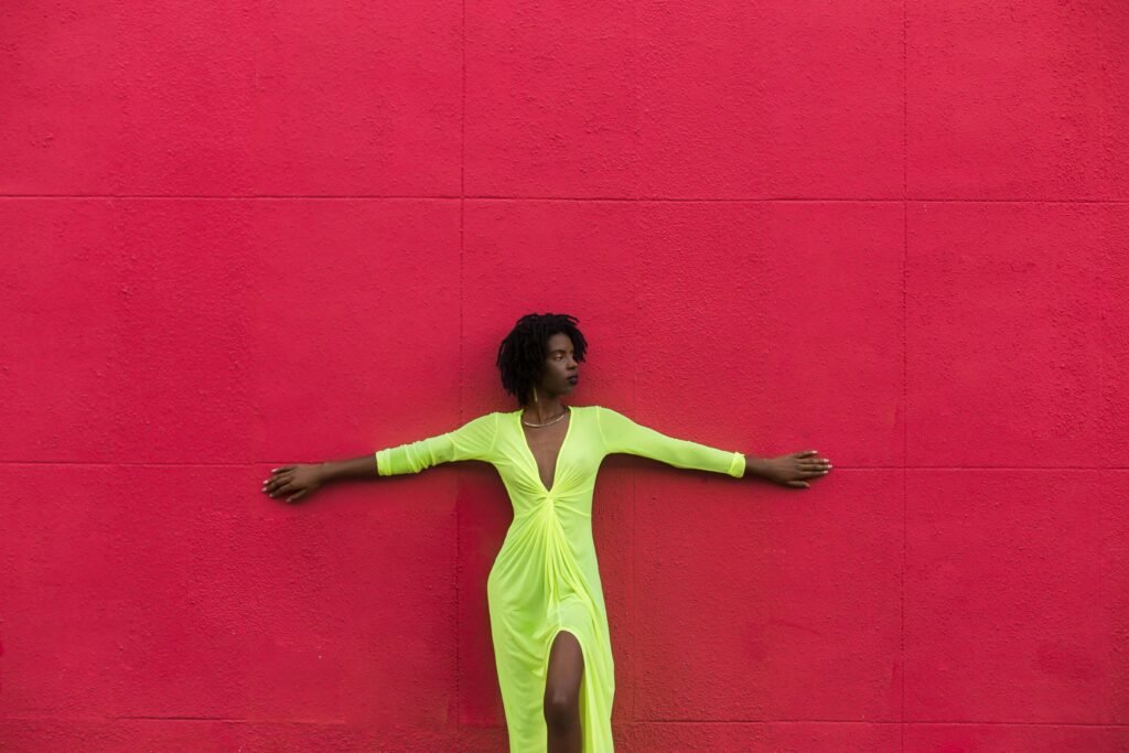 Stylish woman in a green dress posing against a bold red wall, showcasing modern fashion.