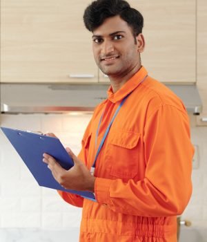Portrait of content young Indian repairman in orange bodysuit making notes in clipboard while inspecting house
